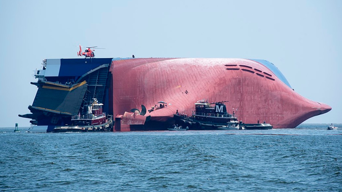 A Coast Guard Air Station Savannah MH-65 Dolphin helicopter rests on the side of the Golden Ray, a 656-foot vehicle carrier, to drop off supplies for Coast Guard crews and port partners who attempt to locate and rescue the remaining four crewmembers aboard the Golden Ray, Sept. 9, 2019, in St. Simons Sound, near Brunswick, Georgia. A Coast Guard Air Station Savannah MH-65 Dolphin helicopter aircrew, Station Brunswick boat crews and other port partners rescued 20 people the morning of Sept. 8, after it was reported the vessel was disabled and listing. (U.S. Coast Guard photo by Petty Officer 3rd Class Ryan Dickinson)